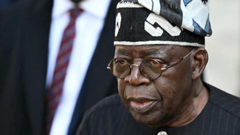 Nigerian leader Bola Tinubu wearing a black gown and hat, as well as glasses