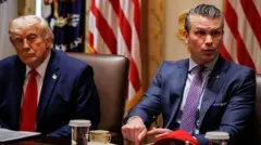 ダークスーツに赤いネクタイを着けたトランプ米大統領と、ダークスーツに紫のネクタイを着けたヘグセス米国防長官が並んで椅子に座り、左の方を見ている