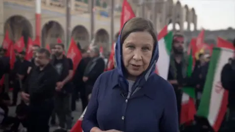 Lyse Doucet looks into the camera as she stands among a crowd carrying Iranian flags
